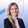 Eine lächelnde Frau mit langen blonden Haaren und blauen Augen trägt einen weißen Rollkragenpullover und ein dunkelblaues Jackett.