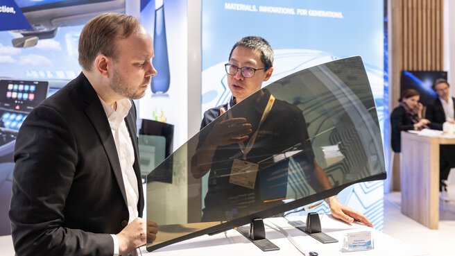 Zwei Fachbesucher begutachten eine transparente Demonstrator-Scheibe am LOPEC Messestand