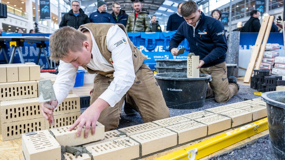 Two people dressed as craftsmen demonstrate how to build a wall to visitors at BAU 2025.