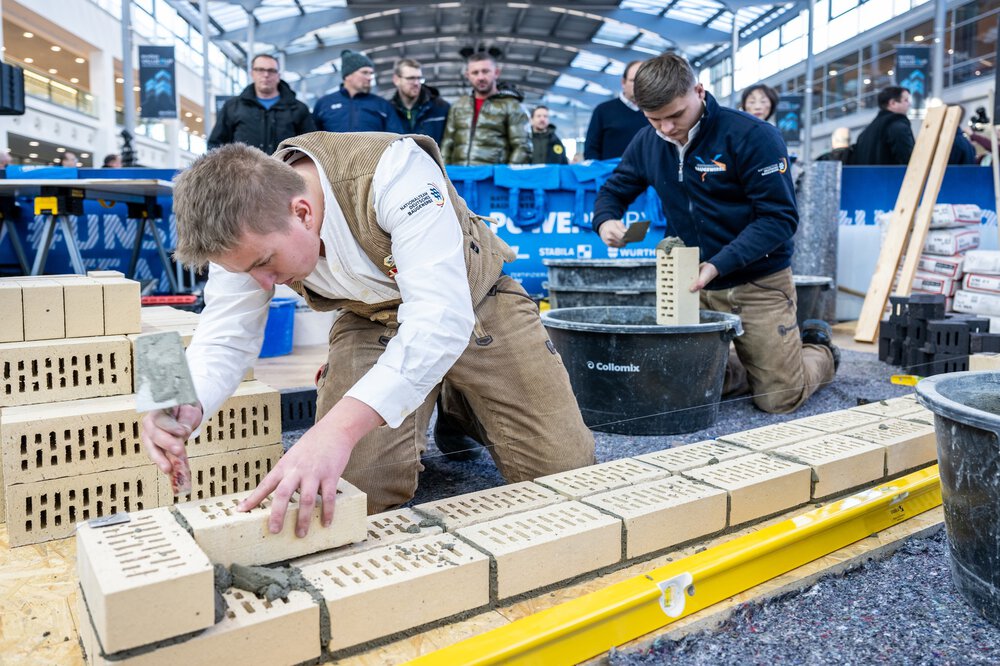 Zwei Personen in Handwerkerkleidung demonstrieren Besuchern der BAU 2025 wie man eine Mauer baut.