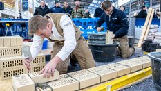 Zwei Personen in Handwerkerkleidung demonstrieren Besuchern der BAU 2025 wie man eine Mauer baut.
