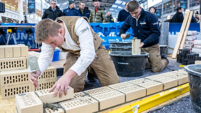 Two people dressed as craftsmen demonstrate how to build a wall to visitors at BAU 2025.