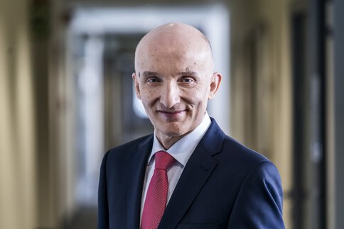 Ein Mann mit Glatze im Anzug mit roter Krawatte lächelt in die Kamera.