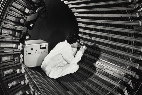 A person in a lab coat sits in a tubular metal structure and inspects the surface with scientific equipment.