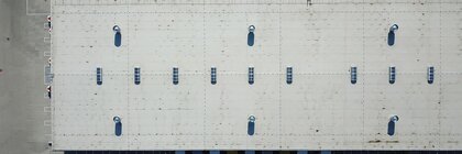 A view from above of a large grey warehouse roof with numerous delivery bays for lorries and lorries parked in reverse alongside the warehouse.
