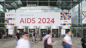 Menschen gehen an einem Eingang mit einem großen AIDS 2024-Banner auf dem Gelände der Messe München vorbei.