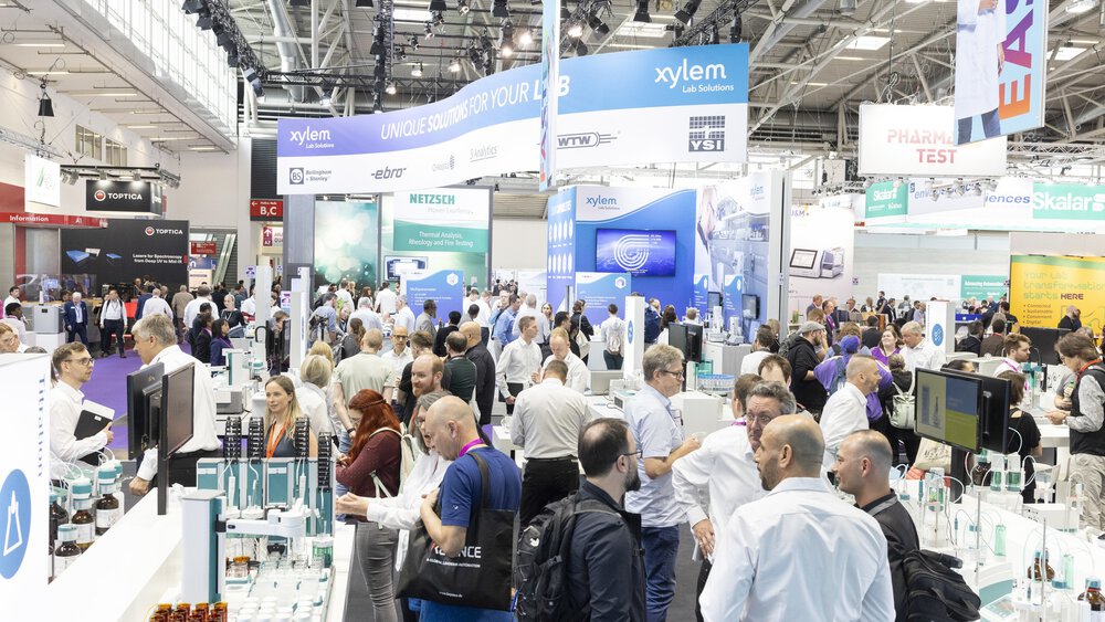 Crowded analytica exhibition hall with busy visitor traffic, laboratory and analytical technology booths, and large overhead banners.
