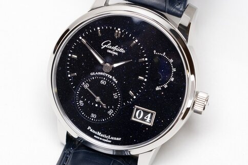 Nahansicht einer filigranen Armbanduhr mit schwarzen Bändern, Ziffernblatt mit Sternenhintergrund und einer Tagesanzeige.