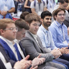 A group of people in business attire sit clapping in the audience of a conference.