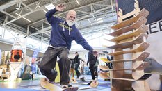 Ein Mann balanciert auf einem Balance-Board an einem Messestand. Rechts neben ihm steht ein Aufsteller mit weiteren Boards aus Holz.