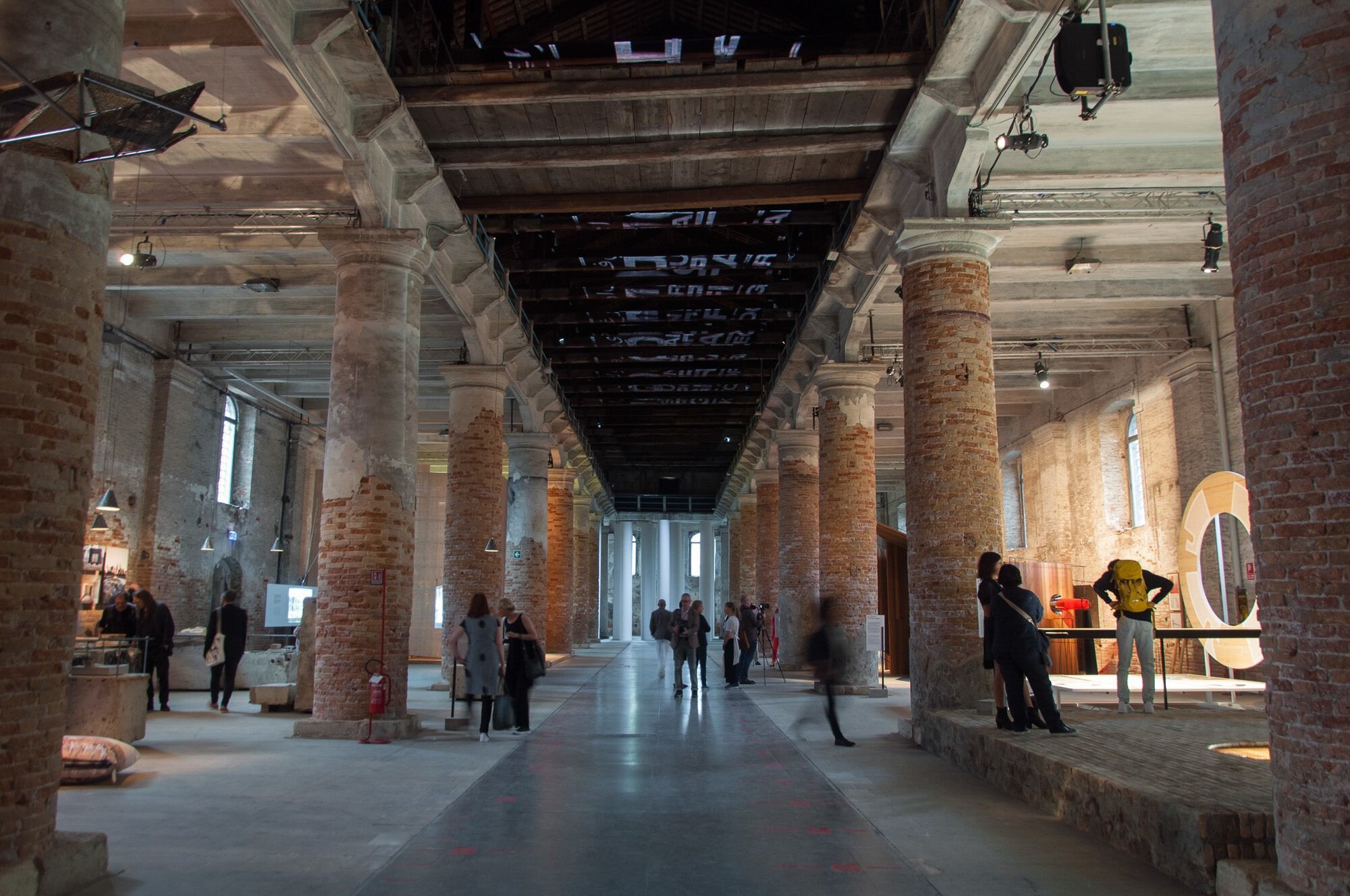 Brick hall with high columns, museum exhibitions and people walking around.