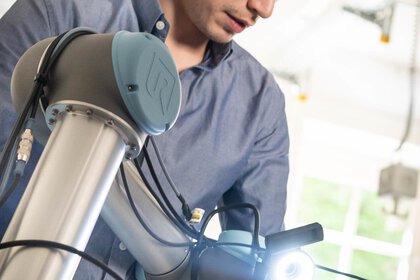 Person in blue shirt inspects the gripper of a robot arm in the interior.