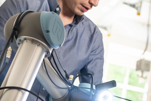 Person in blue shirt inspects the gripper of a robot arm in the interior.