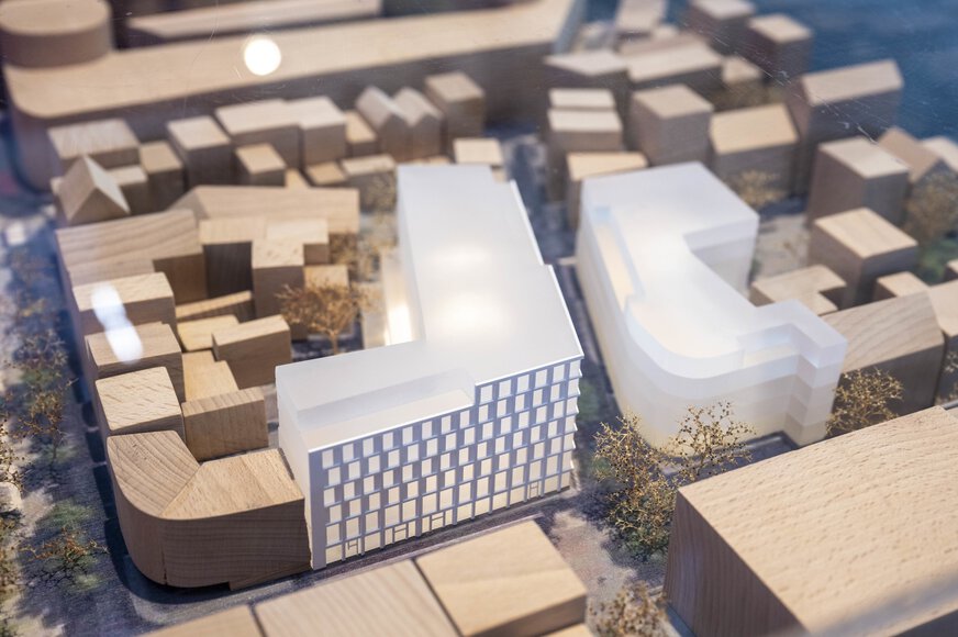 A detailed architectural model of an urban development project displayed at EXPO REAL in Munich. The model is made of wood and plastic elements, depicting buildings, streets, and trees in a city district. In the foreground, two modern, light-colored building complexes with clean geometric shapes are visible.