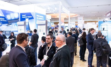 Trade visitors networking at booths showcasing conductive polymers and printed electronics at LOPEC