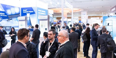 Trade visitors networking at booths showcasing conductive polymers and printed electronics at LOPEC