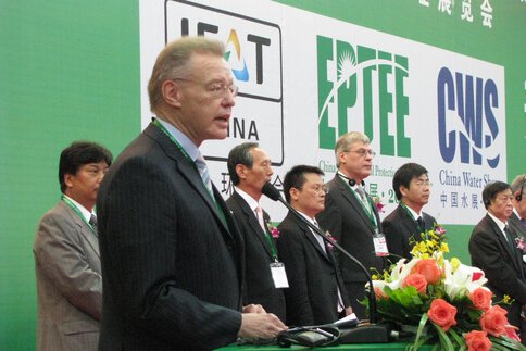 The then managing director of Messe München International, Eugen Egetenmeier, speaks at a lectern at the opening of IFAT China. Behind him on stage is a row of men.