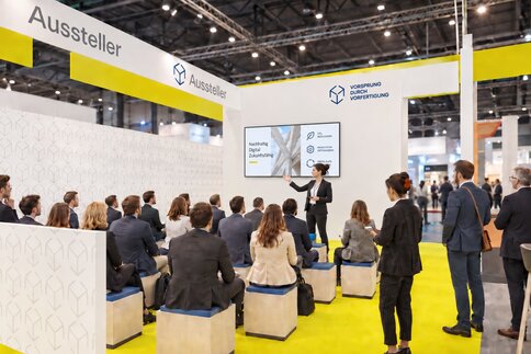 Precast Areana - eine Gruppe von Personen sitz auf einem Messestand und hört einem Vortrag zu