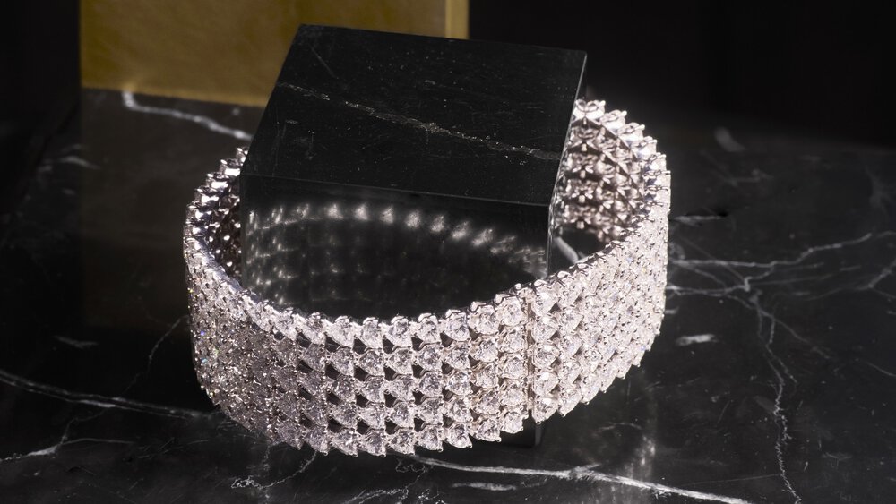 A sparkling diamond bracelet on a black marble surface with a black and gold background.