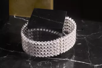 Ein funkelndes Diamantarmband auf einer schwarzen Marmoroberfläche mit schwarz-goldenem Hintergrund.