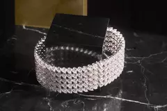 Ein funkelndes Diamantarmband auf einer schwarzen Marmoroberfläche mit schwarz-goldenem Hintergrund.