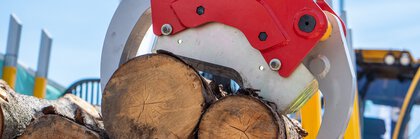  Close-up of red hydraulic loading tongs reaching into a stack of several cut logs.