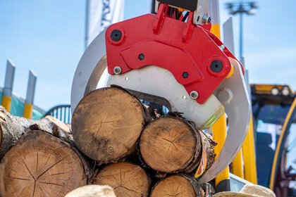 Close-up of red hydraulic loading tongs reaching into a stack of several cut logs.