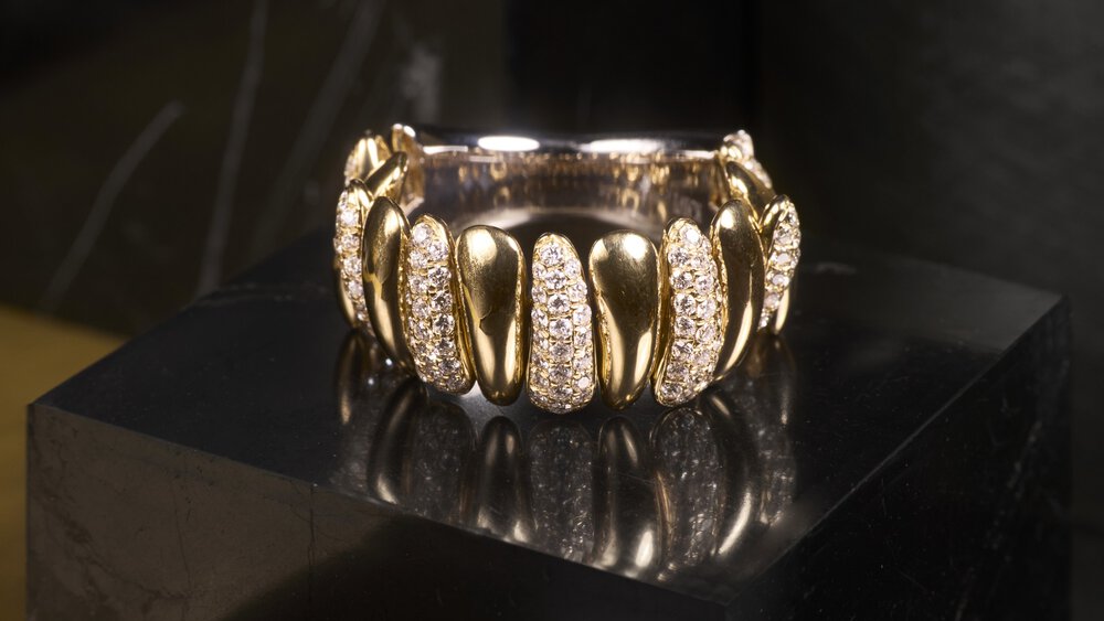 Gold ring with diamond-set segments on a shiny black surface.