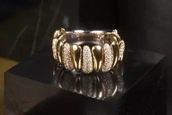 Goldring mit diamantbesetzten Segmenten auf schwarzer, glänzender Oberfläche.