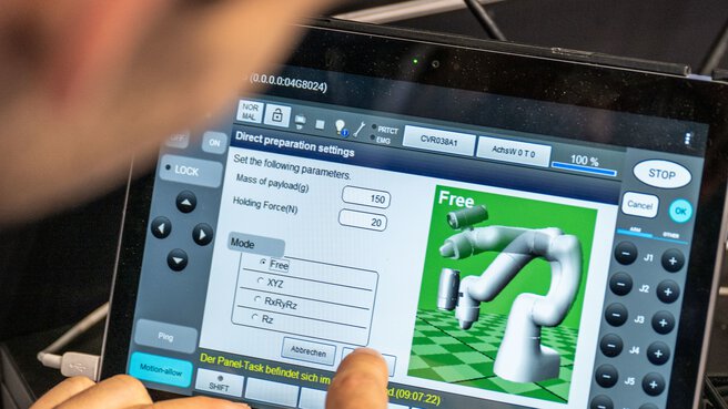 Hand operates a touchscreen to control a robotic arm with a graphical user interface and setting options.