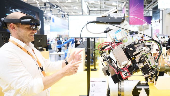 Messebesucher steuert mit AR-Brille ein robotisches Exponat auf der Laser World of Photonics 2025 in München.