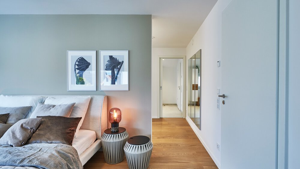 Modernes Schlafzimmer mit einem Bett, braunen Kissen, Wandkunst, zwei Nachttischen, einer Lampe und einem Flur, der zu einer Tür führt.