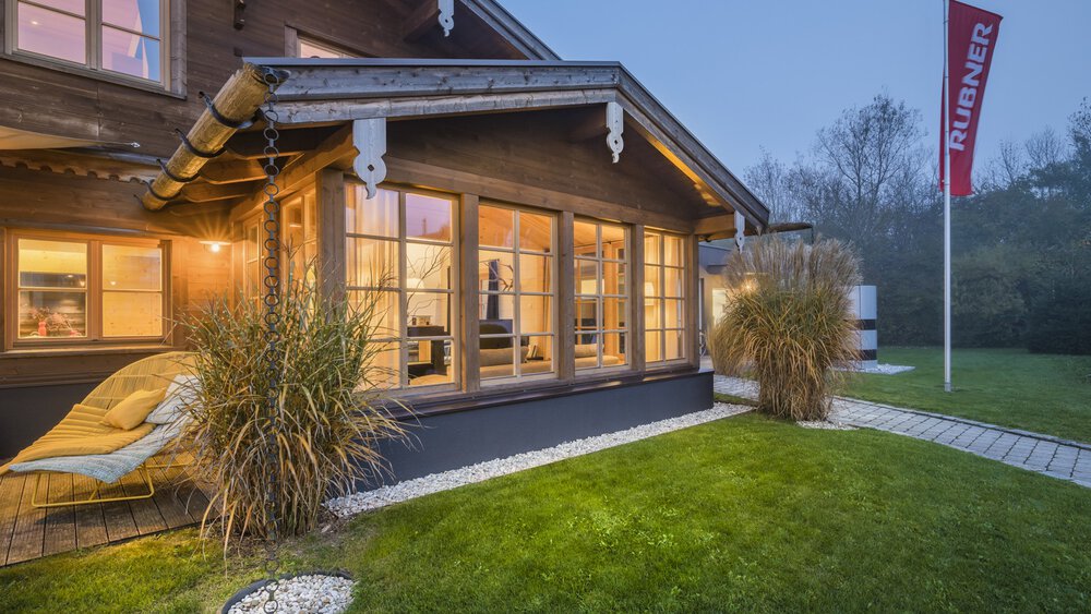 Ein gemütliches, modernes Haus mit großen Fenstern und einem schrägen Dach, umgeben von einem üppigen grünen Rasen und einem Fahnenmast.