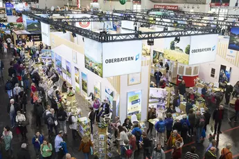 Bird's eye view of a large exhibition stand on the subject of Upper Bavaria in an exhibition hall with many visitors.