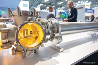 Close-up of a large industrial metal chamber on the LAS with blurred visitors in the background.