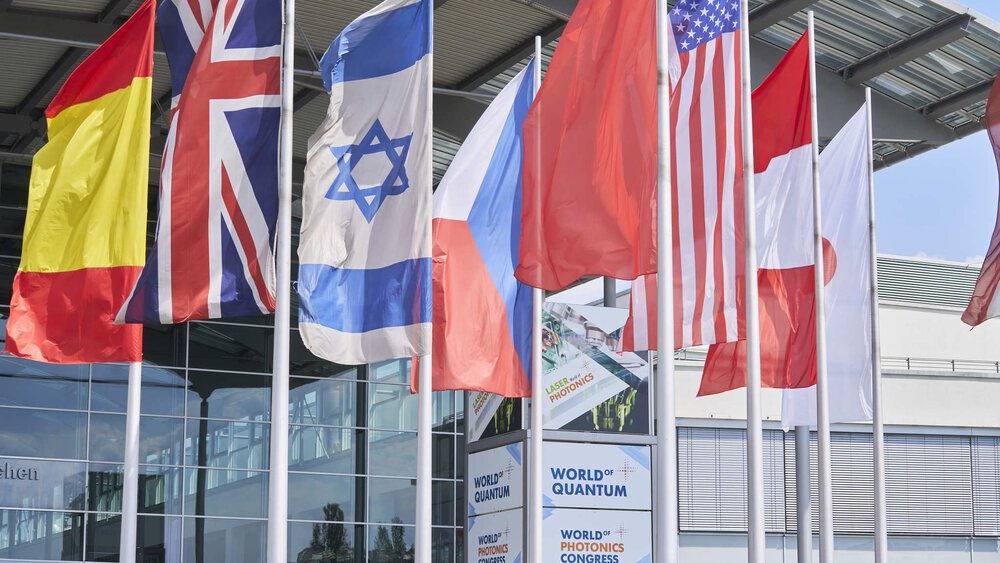 Flags of different countries in front of the exhibition entrance hall. In between are logos of Laser World of Photonice, World of Quantum and World of Photonics Congress.