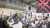 Presentation at the Laser World of Photonics trade show in front of an audience, with exhibition booths and a sign reading “Integrated Photonics Area” in the background