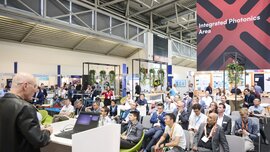 Vortrag auf der Messe Laser World of Photonics vor Publikum, im Hintergrund Messestände und ein Schild „Integrated Photonics Area“