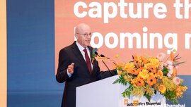 Man giving a presentation at a podium at automatica Shanghai with a slide and floral arrangement in front.