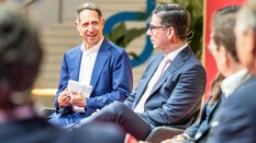 Ein Herr im blauen Anzug sitzt auf der Bühne mit weiteren Talkgästen im Gespräch bei einer Diskussionsrunde der Messe Transport und Logistic 2025.