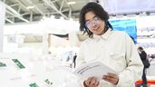A man in a white corduroy shirt stands at an exhibition stand and reads a brochure with the inscription 