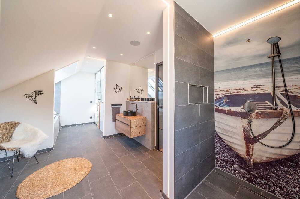 Modernes Badezimmer mit gemütlicher Sitzecke,  Dusche, Waschbecken und dekorativem Raumteiler.