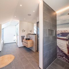 Ein großflächiges Bad mit Dachschräge, einem schwarzen Waschbecken, einer offenen Dusche und einer separat stehenden Badewanne.