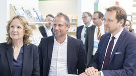 A group of people in business attire are smiling and looking to the left with interest.