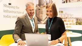 Two people standing at an exhibition stand and looking at a laptop together.