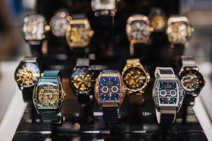 Close-up of luxury wristwatches in various styles and colors on a black stand.