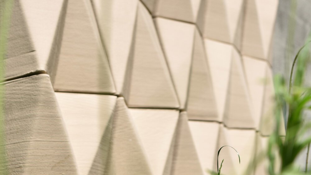 Geometric beige blocks in a mosaic pattern with grass and plants in the foreground.