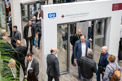 Exhibition stand with automatic sliding doors through which two men are walking.