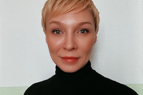 Eine lächelnde Frau mit kurzen blonden Haaren und einem schwarzen Rollkragenpullover.