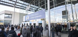 Numerous visitors enter the entrance hall of productronica through the revolving doors of the Messe München main entrance.